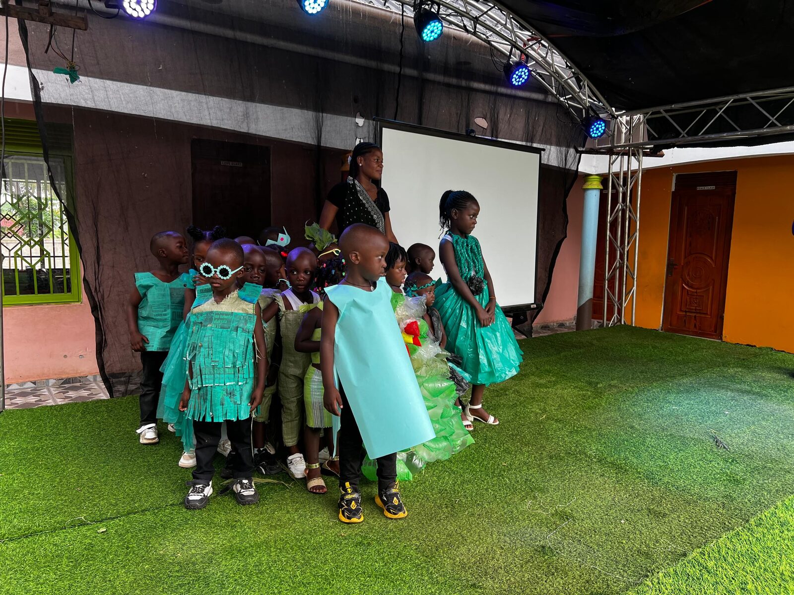 Children wearing costumes made from recycled plastic and paper materials on stage
