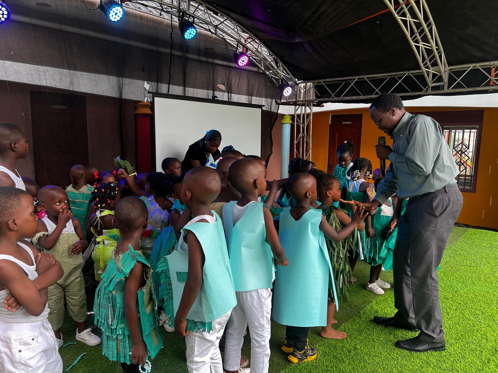 Children in eco-fashion costumes gathered around a staff member with a microphone