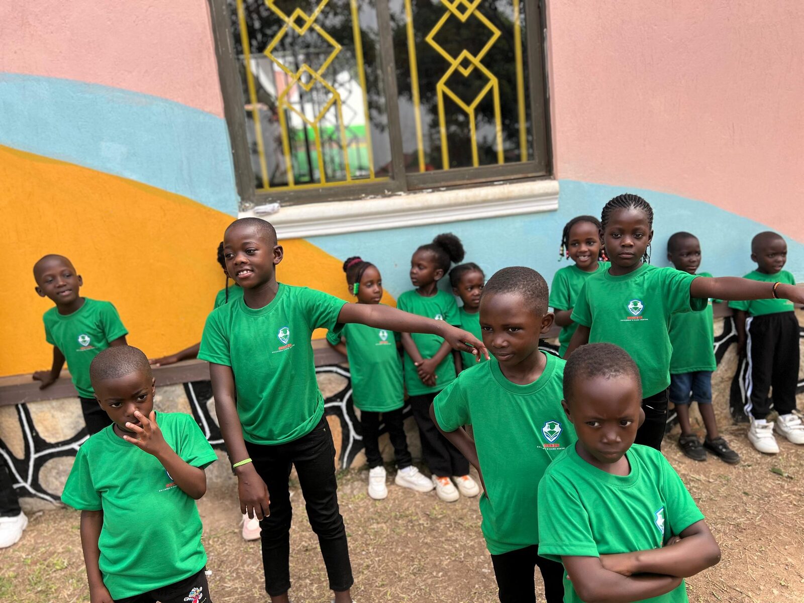 Children in green Goshen Centre shirts posing playfully outside near a colorful mural